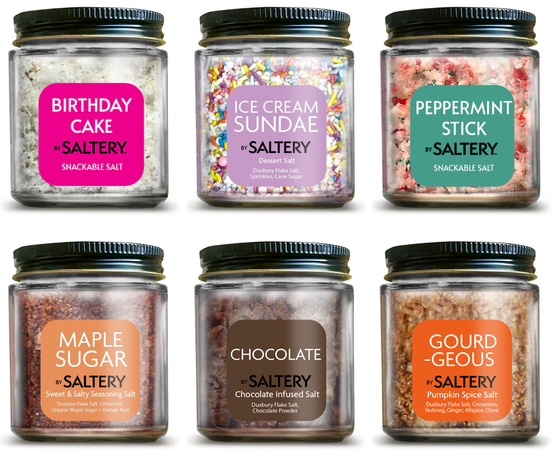 Six clear plastic jars of Saltery snackable salt arranged in a 2x3 grid on a white background. Each jar has a black screw-on lid and a colorful label with a different color and flavor name: Birthday Cake, Ice Cream Sundae, Peppermint Stick, Maple Sugar, Chocolate, and Gourd Geòus.